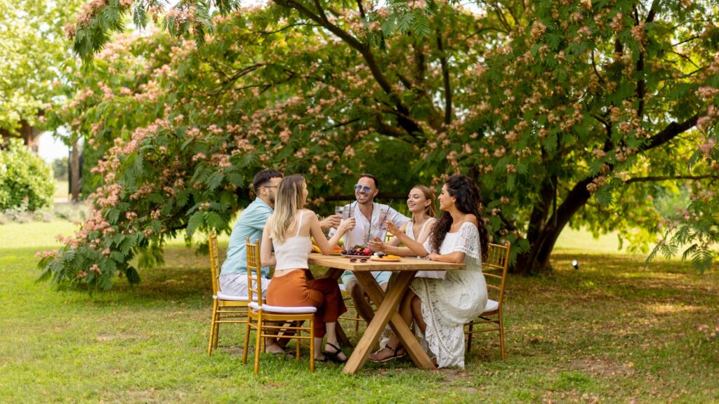 Gruppe glücklicher junger Leute, die mit frischer Limonade jubeln und Früchte im Garten essen