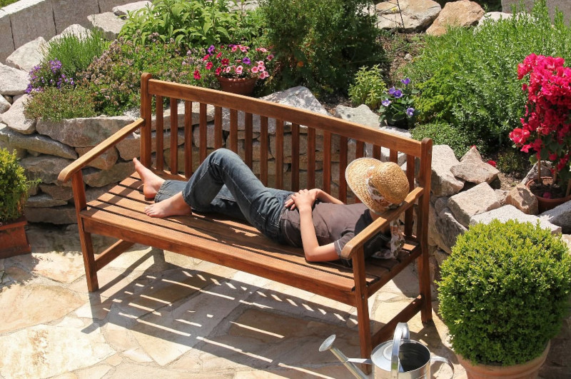 Eine Person liegt entspannt auf einer Holzbank im Garten in Nürnberg und trägt einen Strohhut.